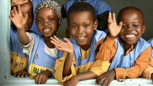 Children inside a classroom smiling and waving their hands