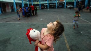 Girl looking at the sky holding her doll in a school serving as shelter in Gaza