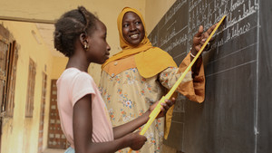 Teacher with student inside a classroom pointing at a blackboard