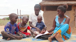 Ajak smiles while looking at a book with children.