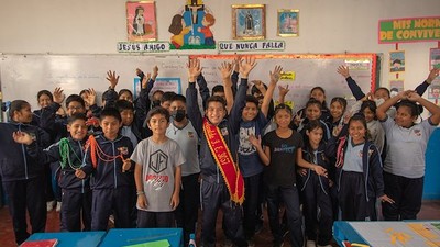 Children inside a classroom smiling and waving their hands