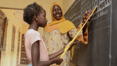 Teacher with student inside a classroom pointing at a blackboard