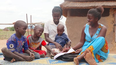 Ajak smiles while looking at a book with children.