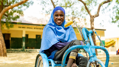 Girl in her wheelchair smiling to the camera outside her classroom