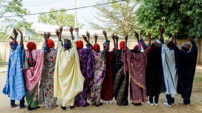 Students raise their hands in front of their school in Nigeria.