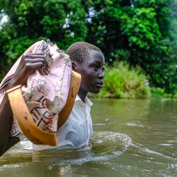 Girl walking through a body of water carrying her schoolbag