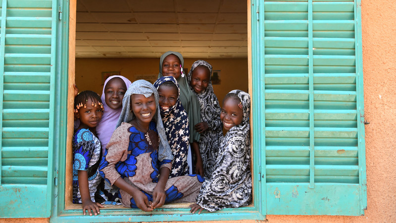 Group of girls in Niger look out a window and smile.
