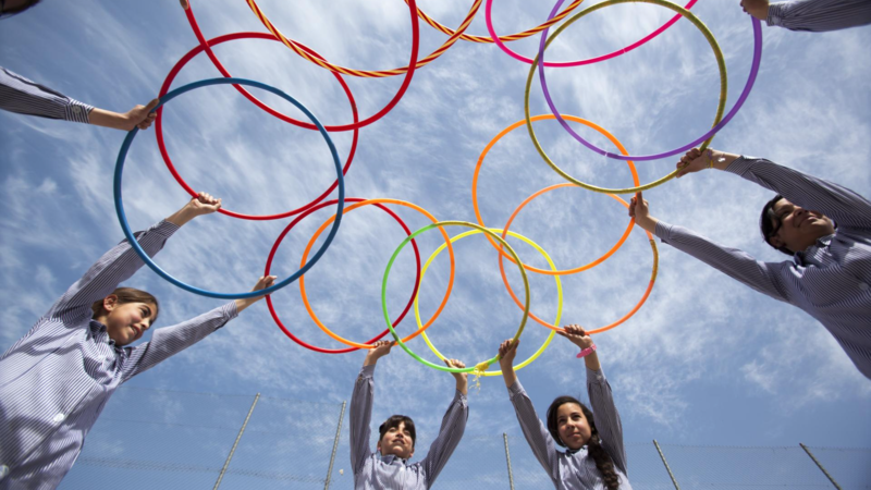 Group of children hold hula hoops to the sky.