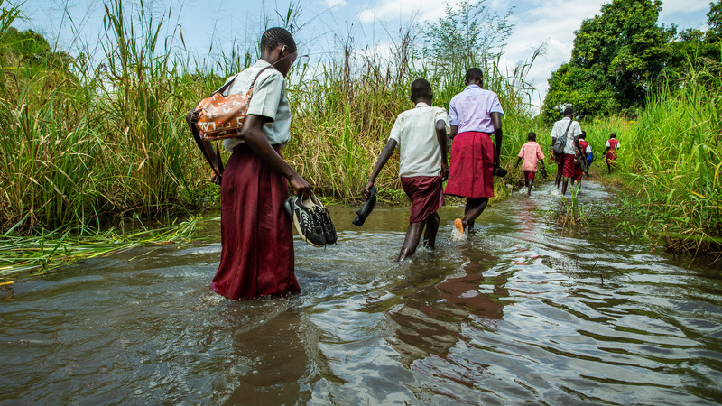 Students in South Sudan walk through flood water.