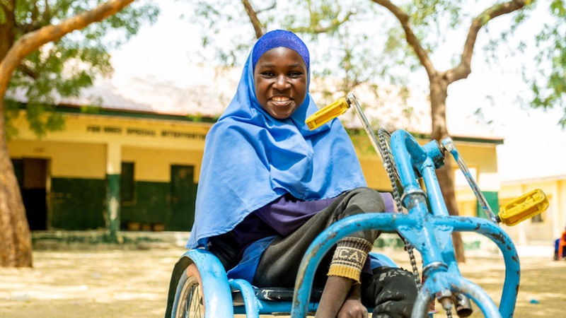 Girl in her wheelchair smiling to the camera outside her classroom