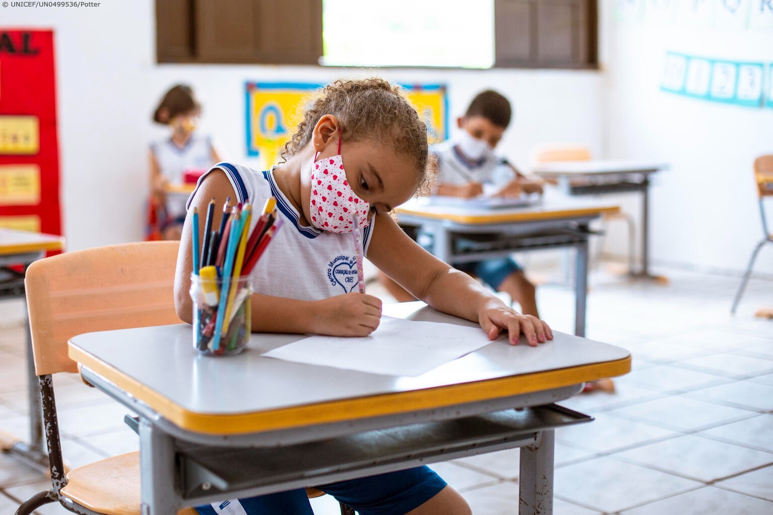 Girl drawing in her classroom while wearing a facemask.